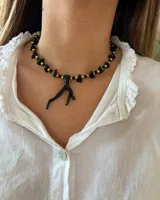 Collar corto con cuentas de piedra irregulares negras y cuentas doradas, con dije colgante en forma de rama negra.