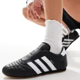 Championes Adidas modelo Taekwondo, color negro con las tres bandas características en blanco. Presentan un diseño sin cordones con empeine acolchado y suela de goma color caramelo.