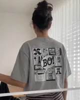 Remera gris de corte regular con estampa gráfica en la espalda que presenta un collage de estilo cómic con la palabra 'BO!' en el centro.
