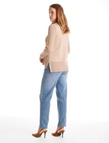 Buzo de punto color beige con cuello volcado amplio, mangas largas acanaladas y torso liso. Presenta una costura central vertical, ruedo con tajos laterales y largo asimétrico, siendo más largo en la parte posterior.