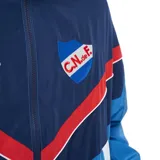 Campera deportiva Umbro del Club Nacional de Football, modelo Beat. Diseño con cierre frontal, cuello alto y bloques de color en azul marino, celeste, rojo y blanco, con el escudo del club y el logo de Umbro bordados en el pecho.