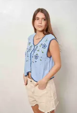 Chaleco celeste tejido de punto con diseño de flores bordadas, escote en V y cierre frontal con botones claros. Presenta detalles de terminación festoneada en tono azul oscuro.