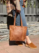 Cartera tipo tote de cuero color camel, con diseño estructurado, costuras decorativas laterales y doble asa superior para el hombro.