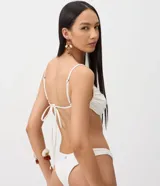 Top de bikini blanco con diseño de media taza, breteles finos y detalle de aplique frontal con forma de concha.