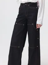 Pantalón de tiro medio y pierna ancha confeccionado en denim de algodón grueso. Presenta un diseño a rayas verticales en tonos azul y celeste, con costuras en contraste color rojo, bolsillos laterales tipo cargo y remaches metálicos.