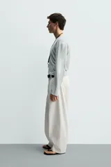 Pantalón barrel fit de hombre, confeccionado en denim de algodón color crudo. Presenta cintura con pliegues frontales, bolsillos laterales y cierre con cremallera y botón.