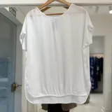Blusa de manga corta color blanco, de corte holgado, con escote redondo y dobladillo curvo con detalle fruncido en la parte inferior.