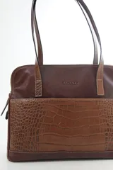 Cartera de hombro tipo portafolio confeccionada en cuero vacuno, con diseño estructurado que combina marrón liso y un panel frontal en cuero texturizado color mostaza. Posee doble asa larga y cierre superior.