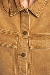 Chaleco de jean tostado con efecto lavado, cuello camisero, cierre frontal con botones metálicos y bolsillos delanteros con solapa. Diseño sin mangas y corte al cuerpo.