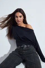 Top de manga larga color negro con escote amplio tipo bote, diseñado para usar con los hombros descubiertos. Presenta una silueta entallada y tejido liso con caída suave.