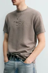 Remera de punto de algodón color gris topo, con efecto lavado, cuello redondo y manga corta. Cuenta con aplicación de parches con texto desgastado en el frente.