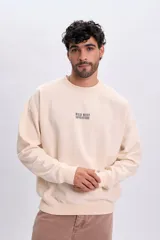 Buzo de felpa oversize color crudo, con cuello redondo y diseño gráfico estampado en la espalda que muestra un paisaje montañoso y un auto con el texto "WILD WEST ADVENTURE".
