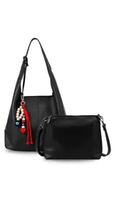Cartera tipo shopper color negro de símil cuero con diseño amplio de hombro, que incluye una bandolera interna desmontable y un llavero amuleto decorativo con cuentas de madera y detalles en rojo.