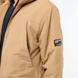 Parka ligera color beige con capucha ajustable, cierre frontal con cremallera y parche decorativo con texto en la manga.