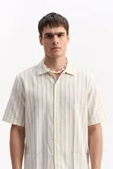 Camisa de manga corta oversize en tejido rústico, con diseño de rayas verticales celestes y blancas, cuello clásico y cierre frontal de botones.
