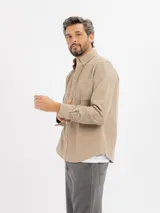 Camisa de pana en color beige, con cuello abotonado, manga larga con puños ajustables y un bolsillo frontal en el pecho.