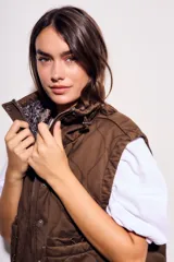 Chaleco reversible de algodón con acabado lavado y diseño acolchado con pespuntes ondulados. Presenta cuello alto con cordón ajustable, cierre frontal de cremallera y botones a presión, bolsillos delanteros tipo parche y cordón de ajuste en el bajo.