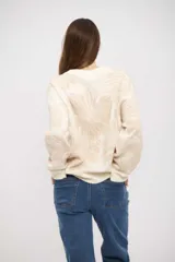 Buzo de tejido de punto con diseño floral en tonos crema y beige, de corte holgado, cuello redondo y mangas largas con puños acanalados.