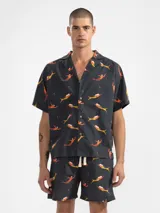Camisa de manga corta con cuello estilo camper y estampado de sirenas en tonos naranja y amarillo. Tiene botones de madera y parche con logo. Corte boxy.