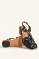 Sandalias de cuero color negro con diseño de tiras cruzadas tipo huarache, tira ajustable con hebilla metálica en el empeine y taco cilíndrico de madera.