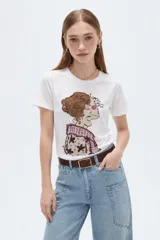 Remera de manga corta color blanco con cuello redondo y ajuste al cuerpo. Cuenta con un estampado frontal ilustrado de una mujer de perfil con detalles de apliques tipo studs.
