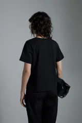 Remera negra de manga corta con detalle de botones metálicos en el hombro. Corte recto y cuello redondo.