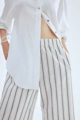 Pantalón tobillero de algodón blanco con rayas verticales finas en negro y beige. Presenta cintura elástica y corte amplio.