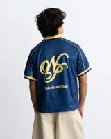 Remera de fútbol estilo vintage de la marca Nude Project, en color azul marino con cuello polo y detalles en amarillo. Presenta inscripciones y un escudo bordado en el pecho.