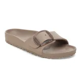 Sandalia tipo pantufla de una sola tira ancha, color topo grisáceo, fabricada en EVA. Presenta una hebilla grande y prominente de color cobre o bronce.