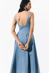 Vestido midi de denim suave, color azul claro, con escote cuadrado, espalda escotada y tirantes anchos. Presenta un cuerpo ajustado y una falda acampanada con frunces en las caderas que aportan volumen.