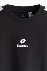 Remera negra de algodón pesado con corte oversized, cuello redondo acanalado, mangas raglán cortas con franja blanca decorativa con el logo de Lotto y logo impreso en el pecho.