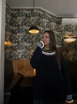 Buzo de punto negro de corte oversize, con cuello babero amplio decorado con franjas de colores y mangas largas con puños terminados en volados en contraste.