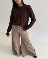 Sweater de punto color marrón chocolate, con cuello redondo y cierre frontal parcial con botones. Presenta mangas largas con puños acampanados y detalle de volados.