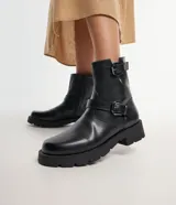 Bota biker negra de caña mediana con hebillas laterales, puntera redonda, cierre lateral y suela track.