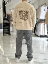 Buzo oversize color beige, con diseño gráfico en la espalda con el texto 'Warm Vibes' en tono marrón y tipografía psicodélica, acompañado de frases secundarias.