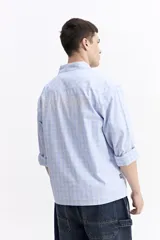 Camisa de popelina a cuadros, color celeste y blanco, de manga larga y corte holgado. Presenta un bolsillo frontal y cartera abotonada.