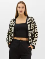 Cardigan abierto de tejido de punto calado con diseño geométrico bicolor en mangas y paneles frontales, y espalda en tono sólido. Presenta silueta recta, frente abierto sin cierre y terminaciones con vivos reforzados en escote, puños y ruedo.