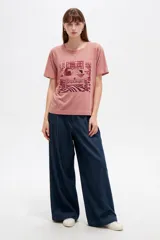 Remera de algodón de manga corta, color blanco, con cuello redondo y estampa frontal de diseño ilustrativo en tonos marrones y fucsia.
