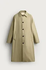 Trench de corte relajado confeccionado en tejido técnico italiano, color beige. Presenta cuello camisero, manga larga, bolsillos de vivo en la cadera y cierre frontal de botonadura simple con botones oscuros.