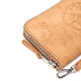 Billetera tipo fichero color habano, confeccionada en material textil con acabado gamuzado. Presenta un diseño rectangular con cierre perimetral decorado con tachas metálicas pequeñas en todo el borde. Incluye una correa de muñeca extraíble y un logo circular grabado en relieve en el centro.