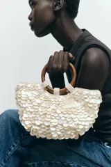 Bolso de mano con forma de media luna cubierto de perlas sintéticas. Tiene asas circulares de madera y detalles de cuentas en la unión con el cuerpo del bolso.