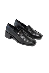 Zapatos tipo mocasín negros con punta cuadrada, confeccionados en cuero liso brillante y un panel central con relieve de charol. Cuentan con un tacón bajo y cuadrado.