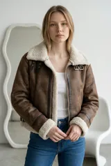 Campera tipo aviador de cuero sintético en color marrón con interior y detalles de corderito sintético en cuello, puños y ruedo. Cuenta con cierre frontal, correas ajustables con hebillas metálicas en el cuello y diseño de costuras reforzadas.