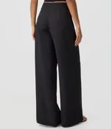 Pantalón sastre negro tipo pantalona, de corte amplio y tiro alto, con cintura lisa, pliegues frontales y cierre lateral invisible.