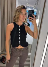 Top sin mangas color negro, con cuello halter y cierre frontal de botones de nácar. El diseño es ajustado y presenta un bajo festoneado.