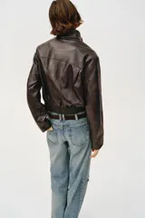 Chaqueta estilo bomber corta de efecto piel en color marrón oscuro, con cuello subido, cierre frontal con cremallera y cintura elástica fruncida.