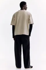 Remera color beige de punto pesado de algodón, de corte holgado, cuello redondo ribeteado y hombros caídos. Presenta estampados en negro en el pecho: el número "33" a la izquierda y un emblema circular con estrellas a la derecha.