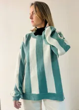 Sweater de punto con diseño de rayas verticales en tonos azul y gris, con sutil acabado brillante. Presenta cuello redondo, mangas largas con puños ajustados y corte amplio con aberturas laterales en el ruedo.