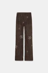 Pantalón de tiro alto color marrón oscuro con cintura elástica y forro interior tipo shorts. Presenta un intrincado bordado de lentejuelas y abalorios en tonos plateados y dorados, formando patrones circulares y figuras de estrellas.