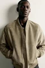 Campera bomber color verde militar de corte relaxed fit, confeccionada en tejido efecto ante, con cuello, puños y dobladillo en rib elástico, bolsillos frontales de vivo y cierre central con cremallera.